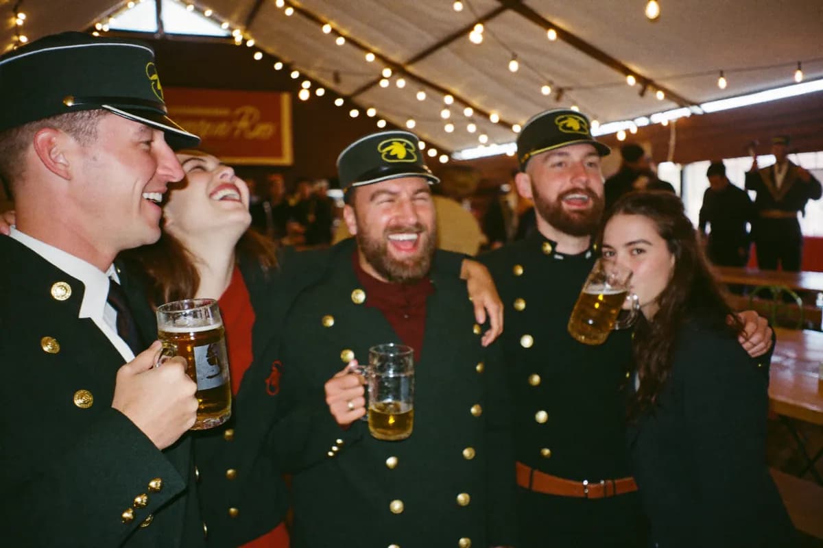 Schützen in grünen Uniformjacken stoßen im Festzelt unter Lichterketten mit Bierkrügen an